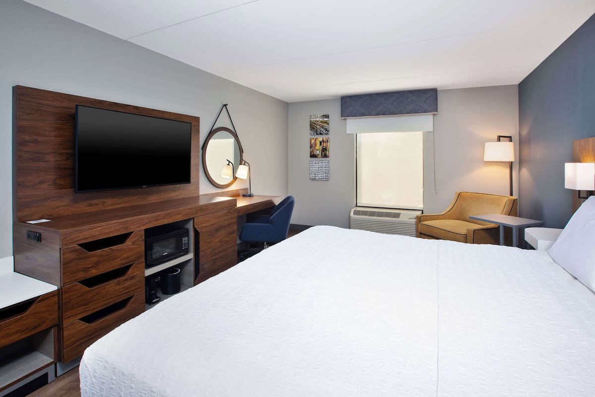 A hotel room with a large bed, a desk with a flat-screen TV, a microwave, a coffee maker, a chair, and a small table.
