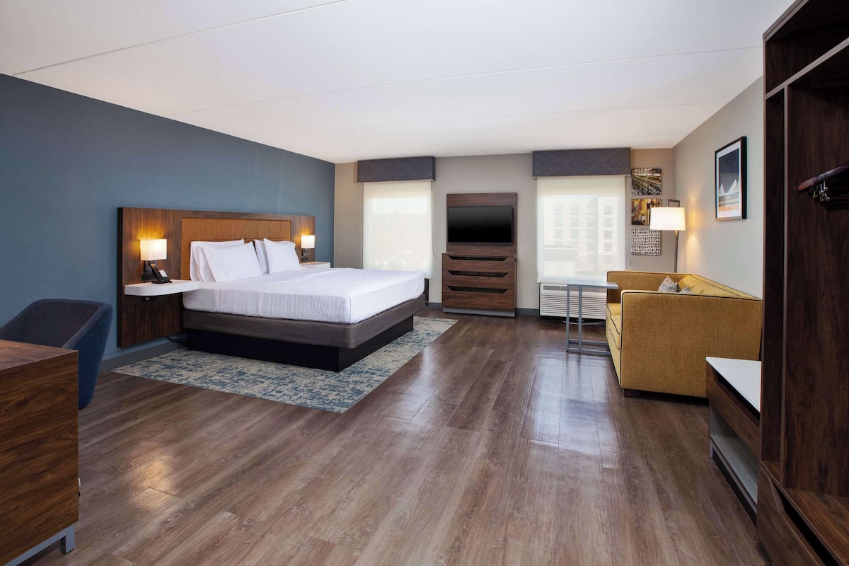 A modern hotel room with a large bed, a sofa, a TV, and a desk.