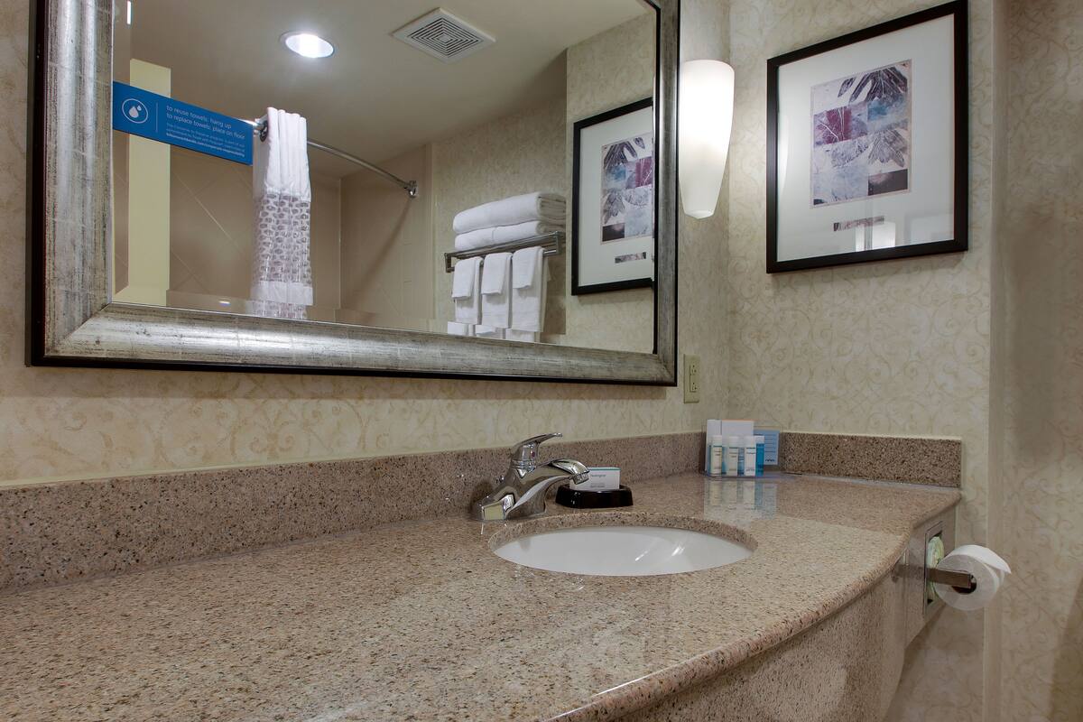 A bathroom with a granite countertop, a sink, a mirror, a towel rack with folded towels, and a framed picture on the wall.