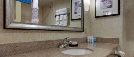 A bathroom with a granite countertop, a sink, a mirror, a towel rack with folded towels, and a framed picture on the wall.