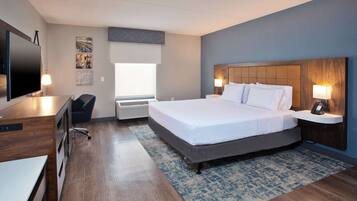 A modern hotel room with a large bed, a desk with a chair, a flat-screen TV, and a window with blinds.