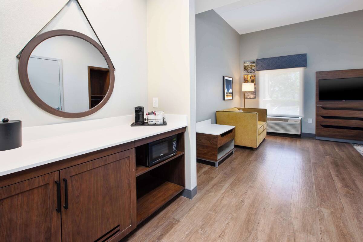 A modern bathroom with a round mirror, a coffee machine, and a microwave on the counter.