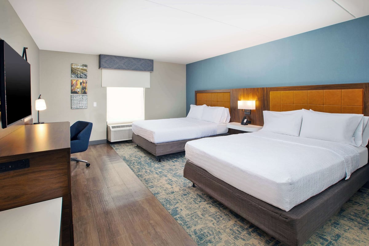 A hotel room with two beds, a desk, a chair, a TV, and a window.