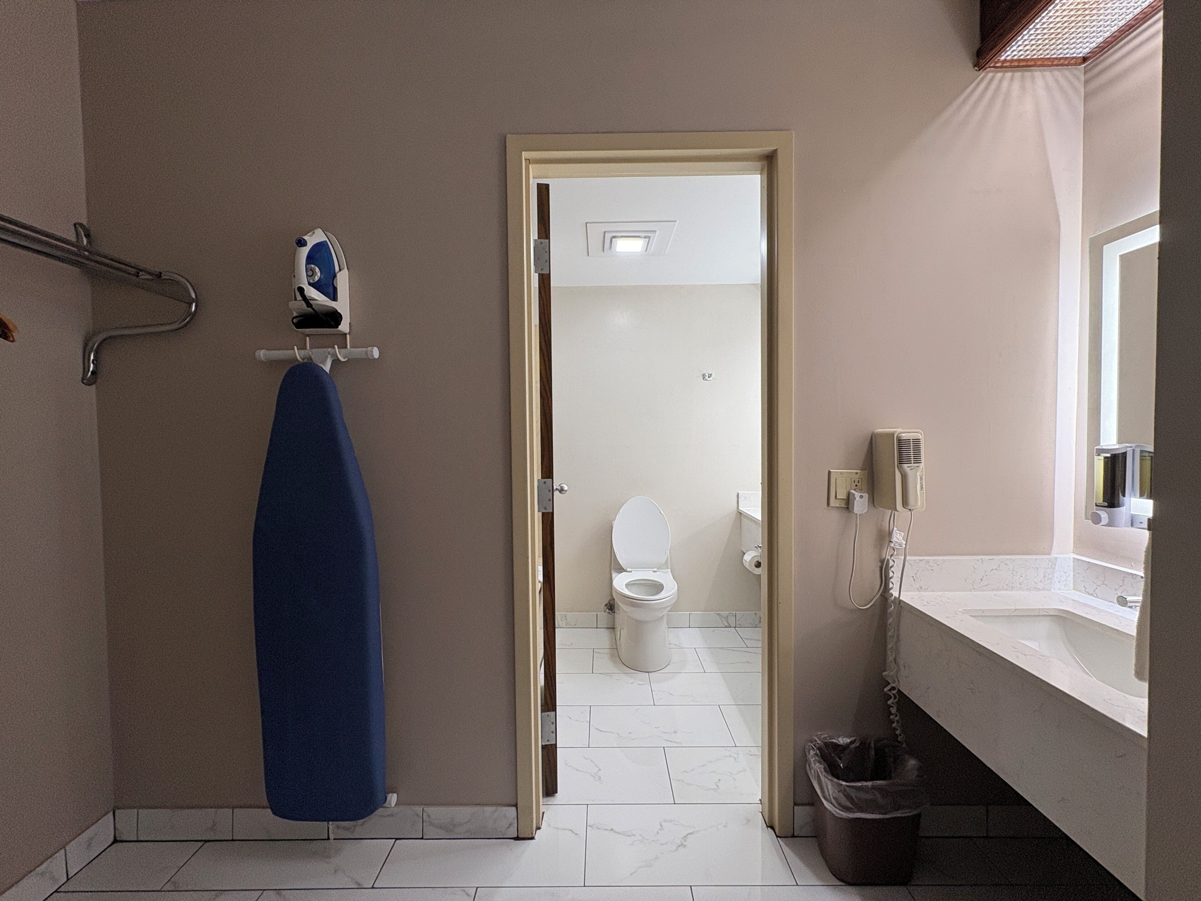 Une salle de bain avec des toilettes blanches, un porte-serviettes avec une serviette bleue, un espace douche et un lavabo avec un miroir.