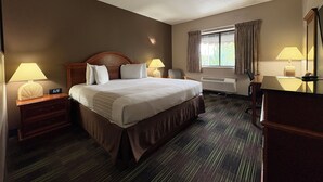 A hotel room with a bed, two bedside tables with lamps, a desk, a chair, a window with curtains, and a mirror. - South Shore Inn (Sandusky)