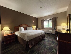 A hotel room with a bed, two bedside tables with lamps, a desk, a chair, a window with curtains, and a mirror. - South Shore Inn (Sandusky)
