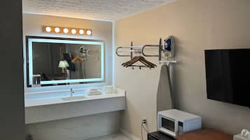Un baño con un espejo grande, tocador, lavamanos, toallero, ducha y un microondas.