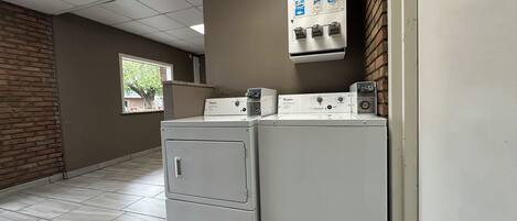 Lavandería con lavadora y secadora Whirlpool, dispensador de jabón, lejía y suavizantes, y una ventana que proporciona luz natural.