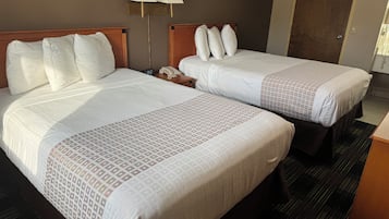 Two double beds with white linens and a patterned bedspread, a bedside table with a lamp, and a wooden headboard.