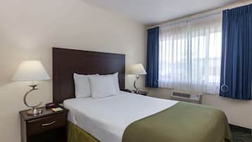 Habitación de hotel con cama, dos mesitas de noche con lámparas, ventana con cortinas azules y aire acondicionado mural.