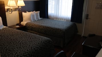 Une chambre d’hôtel avec deux lits, une table de chevet avec une lampe, une horloge numérique et une porte avec une poignée.