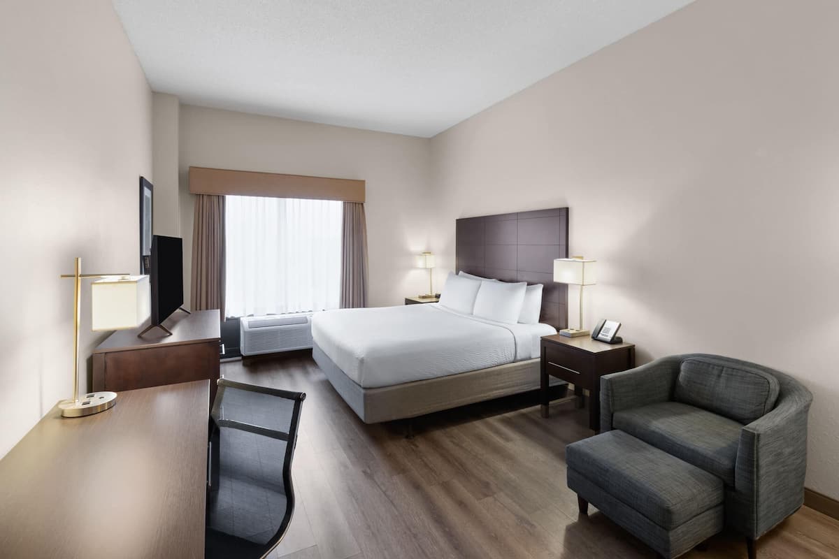 Une chambre d’hôtel avec un lit, un bureau, une chaise, une télévision et une fenêtre avec des rideaux.