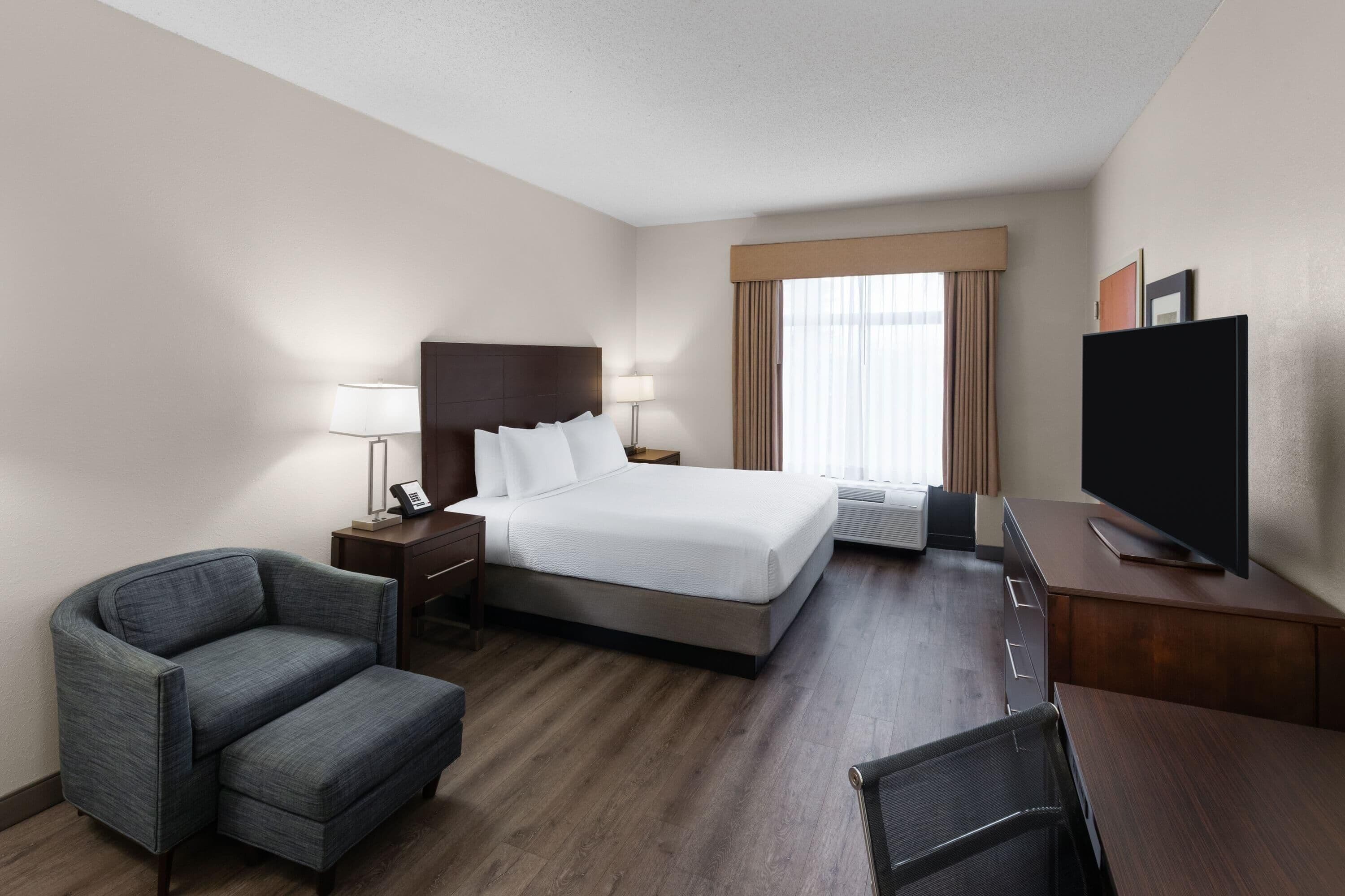 A hotel room with a bed, a desk, a chair, a television, and a window with curtains.