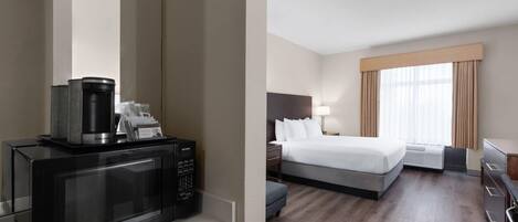 A hotel room with a microwave, a bed, a nightstand, a lamp, and a window with curtains.