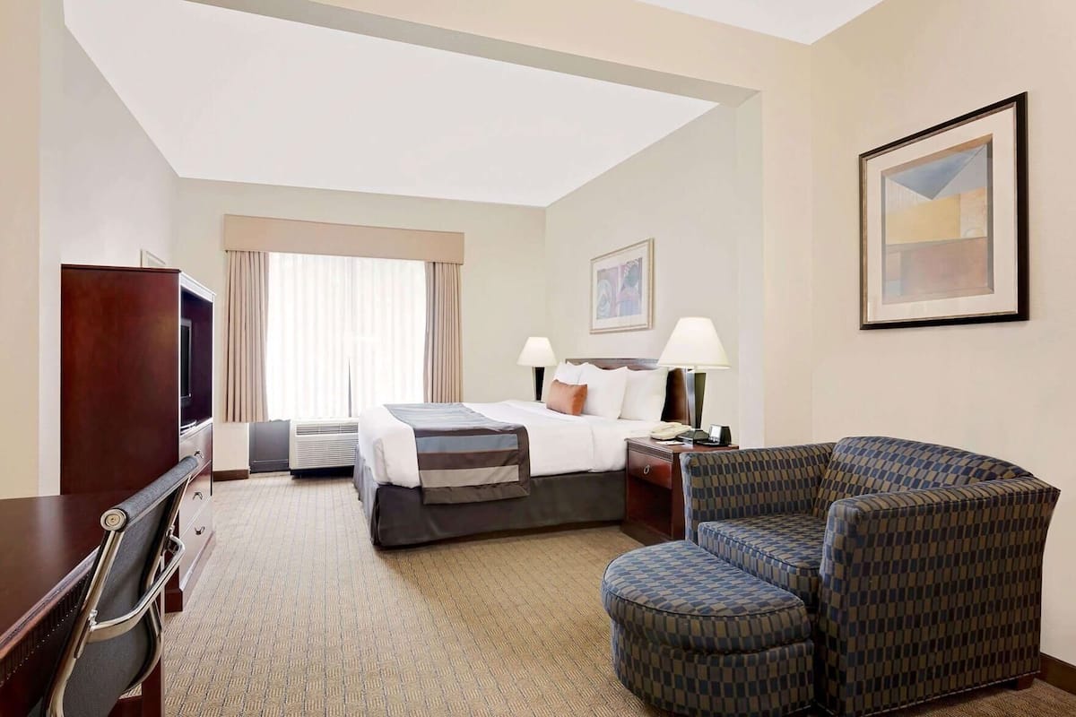 Une chambre d’hôtel comprenant un lit, deux tables de chevet avec des lampes, une télévision, un bureau avec une chaise et un fauteuil à motifs.