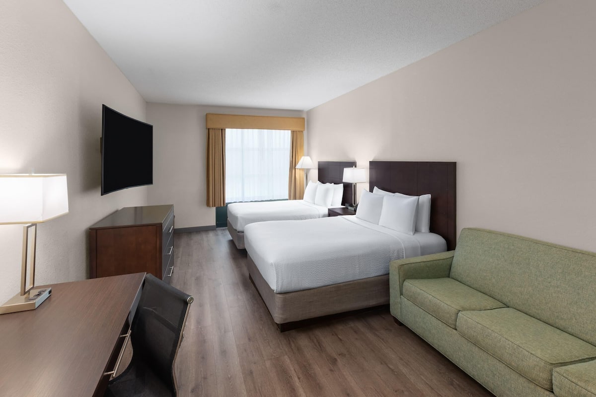 Une chambre d’hôtel avec deux lits, un bureau, une télévision et un canapé vert.