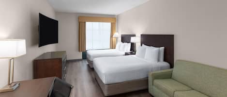 A hotel room with two beds, a desk, a TV, and a green sofa.