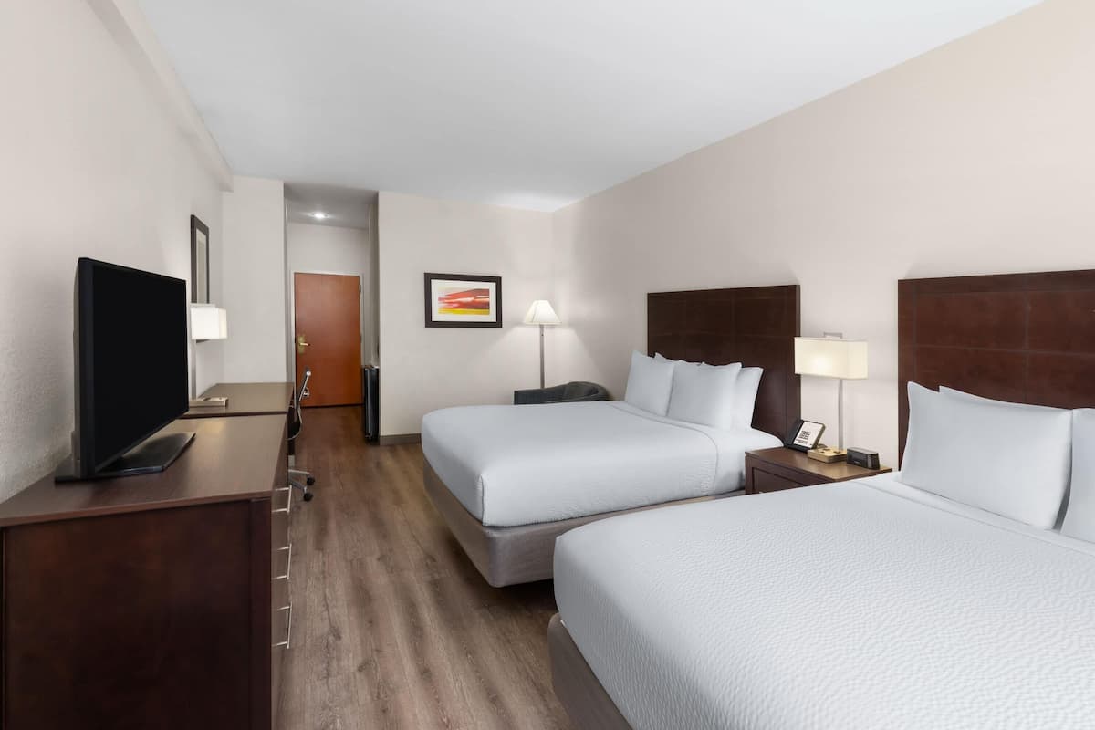 Une chambre d’hôtel avec deux lits, un bureau avec une télévision, des lampes de chevet et une porte visible au fond.