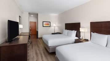 A hotel room with two beds, a desk with a TV, bedside lamps, and a door in the background.