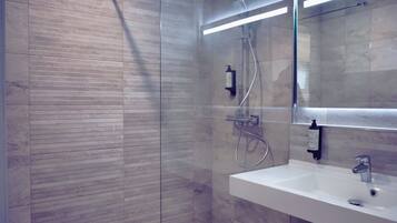 Un baño moderno con ducha de vidrio, un lavabo blanco y un espejo encima.
