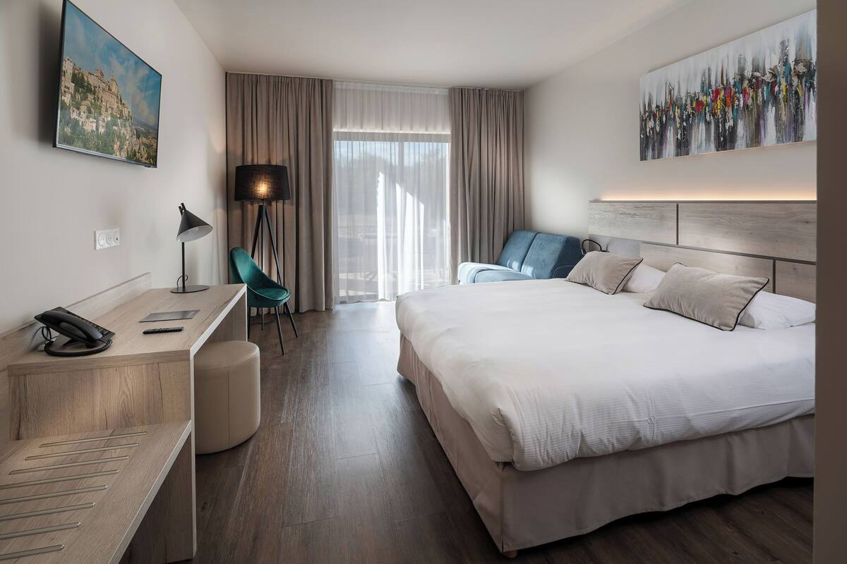 A hotel room with a bed, desk, chair, and artwork on the walls.