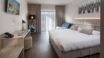 A hotel room with a bed, desk, chair, and artwork on the walls.
