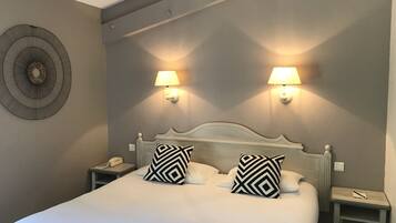 A neatly made bed with two patterned pillows, two bedside lamps, a wall clock, and a decorative wall piece.