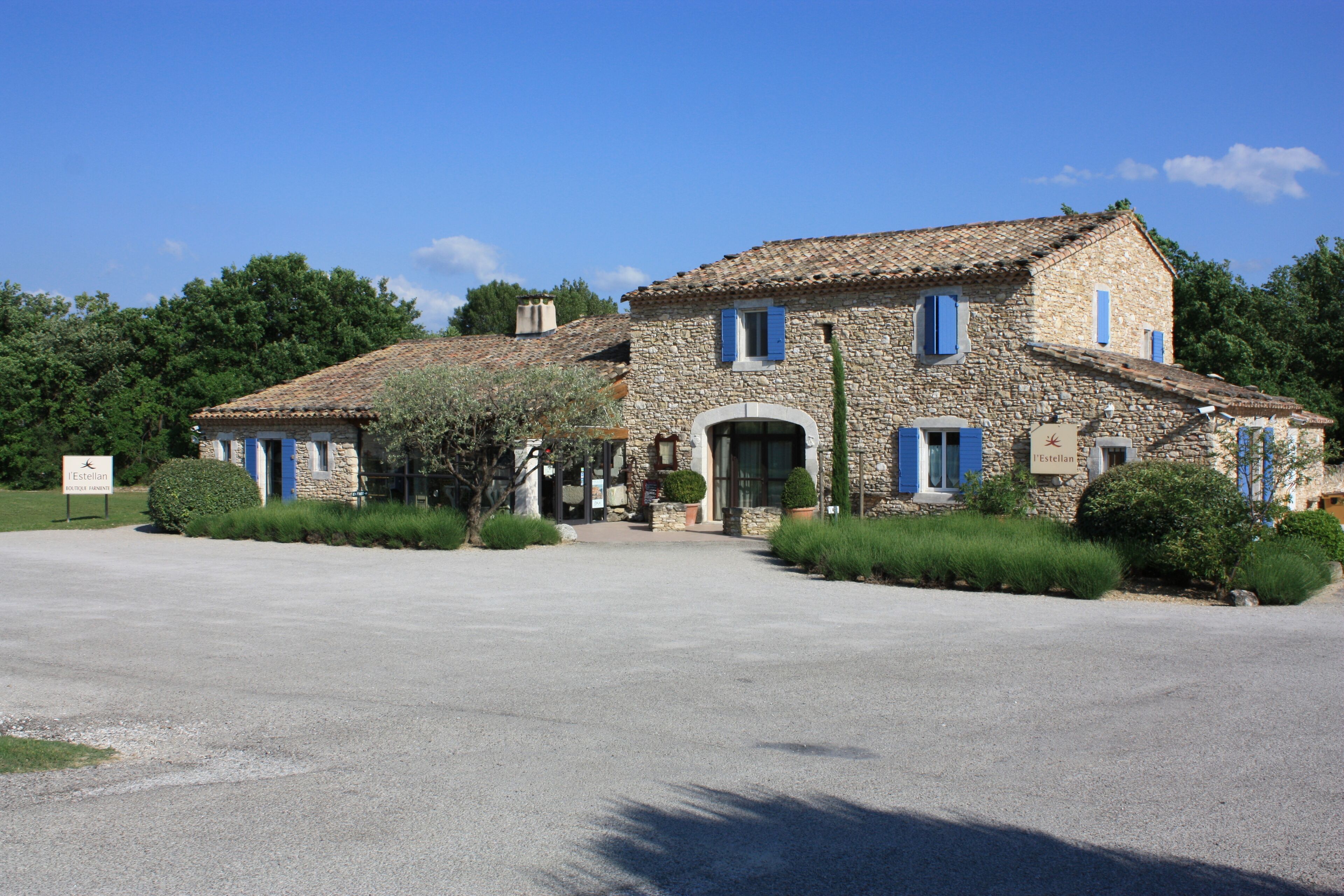 A stone building with a tiled roof, a central entrance, and blue shutters.
