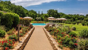 A pathway leading to a pool surrounded by lush greenery and red flowers. - Mas de la Senancole & Spa (Gordes)