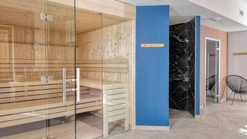 Un área de sauna moderna con paredes de vidrio, bancos de madera y una pared de acento azul.