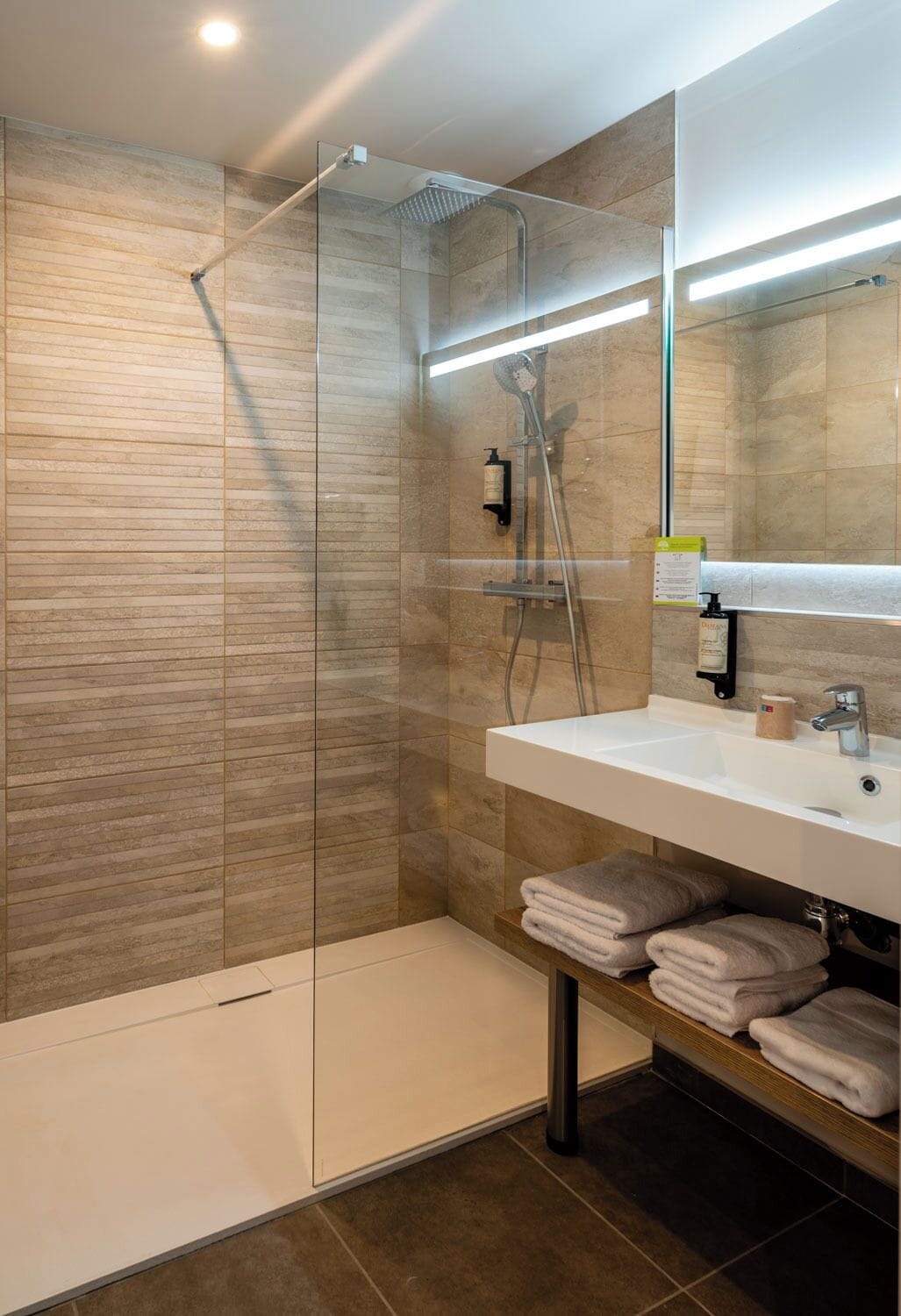 Ein modernes Badezimmer mit einer gläsernen Dusche, einem weißen Waschbecken und einem Spiegel darüber.