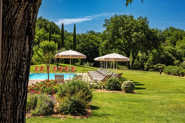 A pool area with lounge chairs and umbrellas, surrounded by well-maintained grass and trees. - Mas de la Senancole & Spa (Gordes)