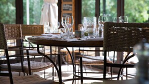 A dining table set with glassware and plates, surrounded by wicker chairs, in a room with large windows and a curtain. - Mas de la Senancole & Spa (Gordes)