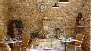 A stone-walled interior with a central fountain, wicker chairs, and tables set for dining. - Mas de la Senancole & Spa (Gordes)