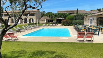 A pool area with lounge chairs and tables, surrounded by stone buildings with tiled roofs.