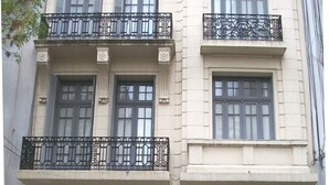 Un immeuble à plusieurs étages, de style architectural classique, caractérisé par des fenêtres disposées de manière symétrique, des balcons en fer forgé décoratifs et une entrée centrale avec une grande porte.