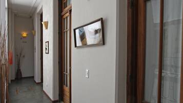 Un pasillo con puerta de madera, un cuadro enmarcado en la pared y una planta en maceta.