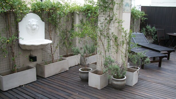 Une terrasse en bois agrémentée de jardinières et un mur en pierre orné d’une sculpture représentant une tête de lion.