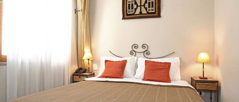 A neatly made bed with a striped bedspread and two pillows, a bedside table with a lamp, and a wall-mounted clock.