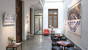 Un couloir orné d’œuvres d’art, une chaise rouge et un espace détente avec des tables et des chaises.