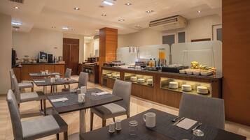 Un comedor de hotel con mesas, sillas, un bufé y un equipo de aire acondicionado.
