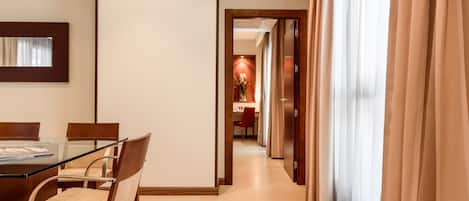 Una habitación de hotel con comedor, un espejo y vista a un pasillo con puerta.