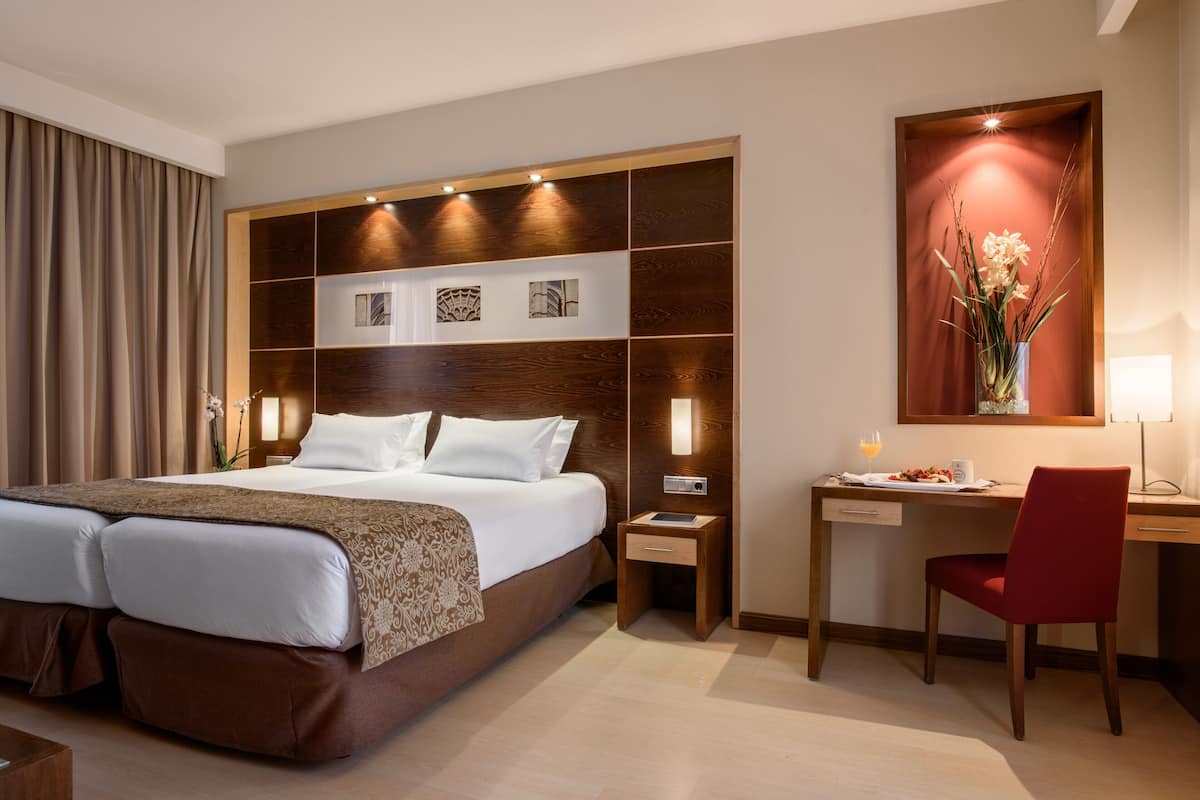 Una habitación de hotel con una cama grande, un escritorio, una silla y una mesita de noche.