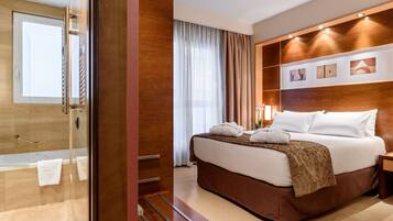 A hotel room with a large bed, a wooden headboard, a glass shower enclosure, and a view of the city.