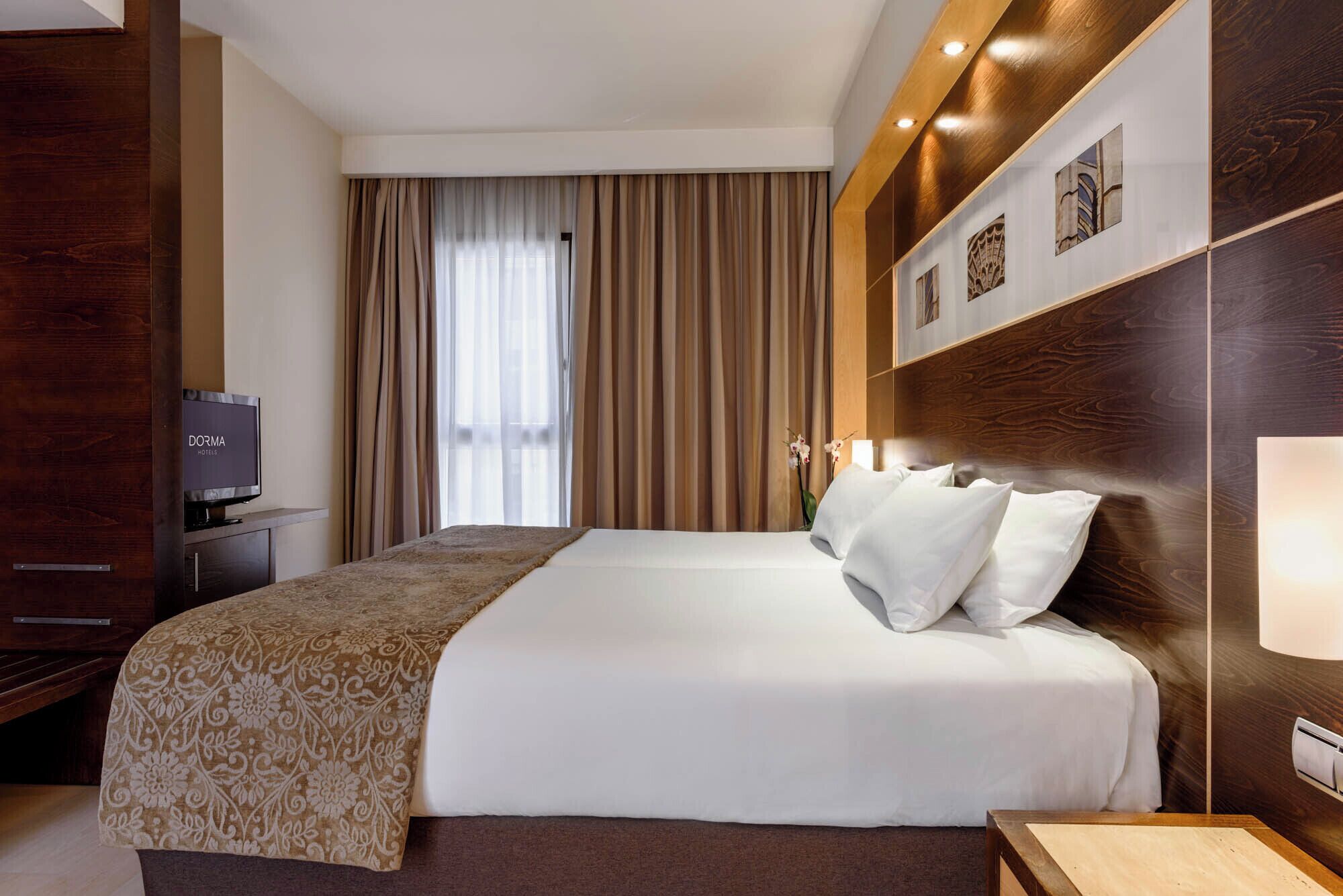 Een hotelkamer met een groot bed, een televisie, een houten hoofdbord en een wandlamp.