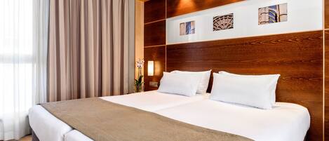 A large bed with a wooden headboard, white bedding, and a brown throw blanket.