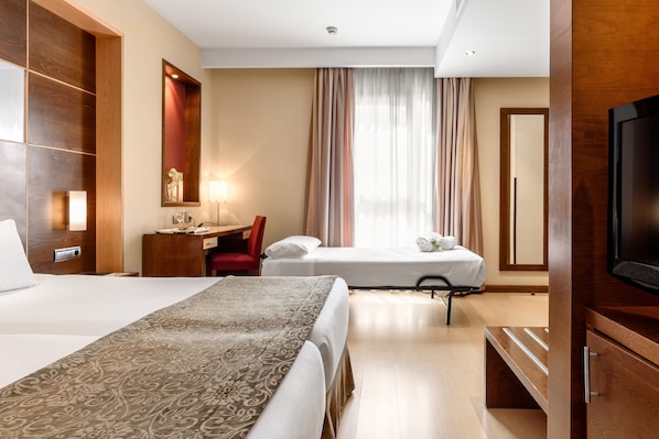 A hotel room with two beds, a desk, a chair, a TV, and a large mirror. - Hotel Dorma León (León)