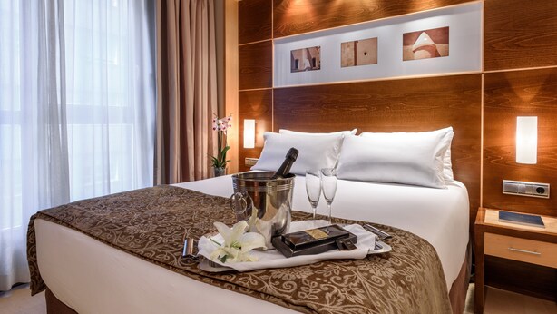 Une chambre d’hôtel avec un grand lit, un minibar, une table de chevet et une étagère murale décorée de tableaux.