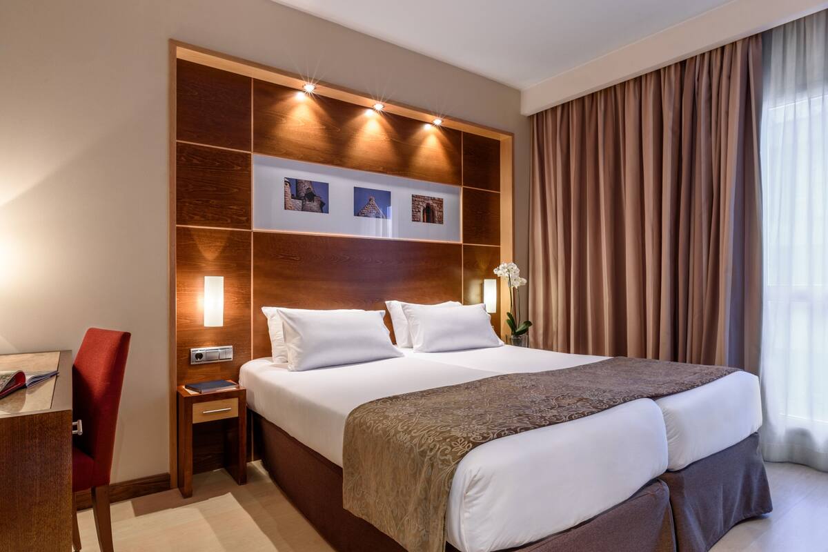 Habitación de hotel con una cama grande, una mesita de noche, una silla roja y un estante en la pared con fotografías.