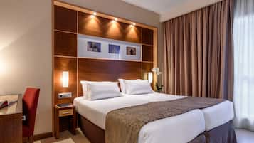 A hotel room with a large bed, a bedside table, a red chair, and a wall-mounted shelf with pictures.